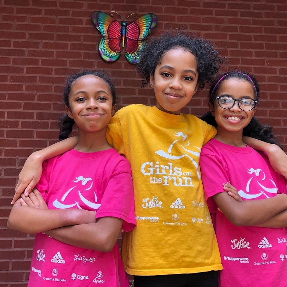 Three happy elementary-aged Girls on the Run participants smiling together