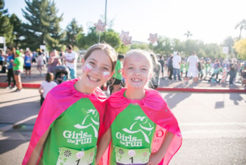 two Girls on the Run participants smile in green GOTR shirts with pink capes